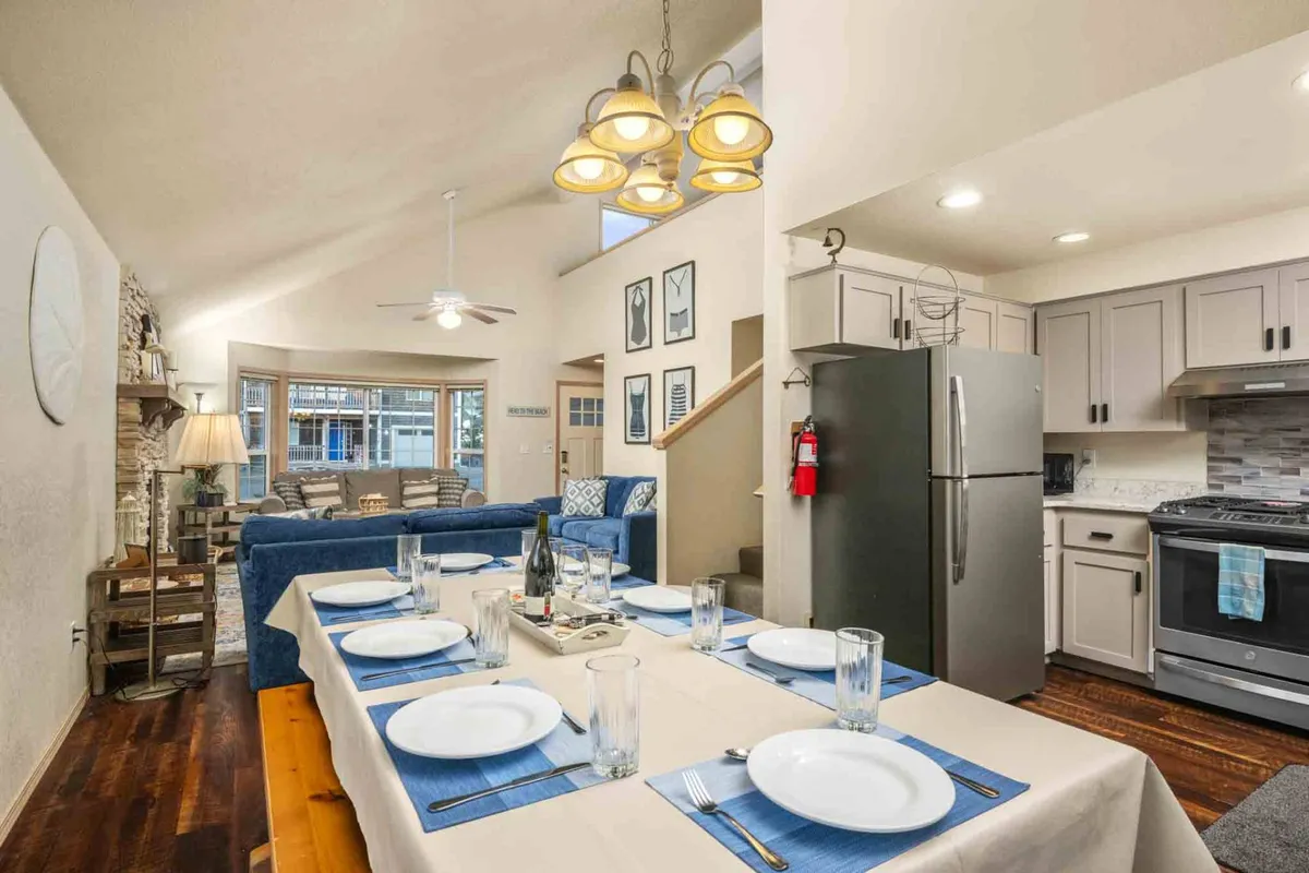 An open-concept space that seamlessly integrates a dining table set for a meal with a comfortable, stylish living area in the background. Decorative wall art and warm lighting enhance the inviting, communal feeling. The layout encourages group dining, conversation, and shared experiences in a single, connected hub.