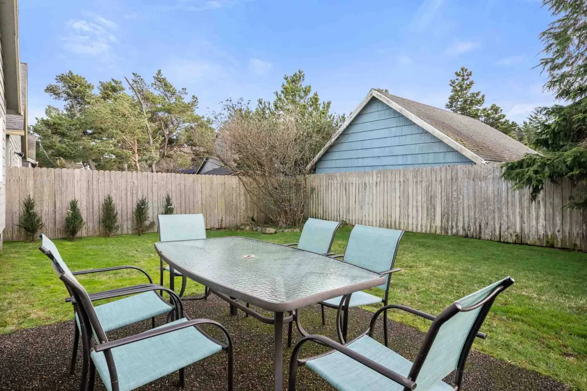 A glass table with metal chairs sits on a patio overlooking a vibrant lawn bordered by a sturdy fence and framed by mature trees. The spacious, open area invites both relaxation and active play, and the fencing ensures peace of mind for families with children.