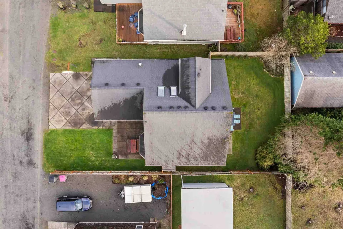 A wide view of the property shows the main house with a backyard deck, generous green lawn, and neighboring homes visible beyond the fence. The open deck invites gatherings and barbecues, while the expansive lawn is perfect for active outdoor games and family time.