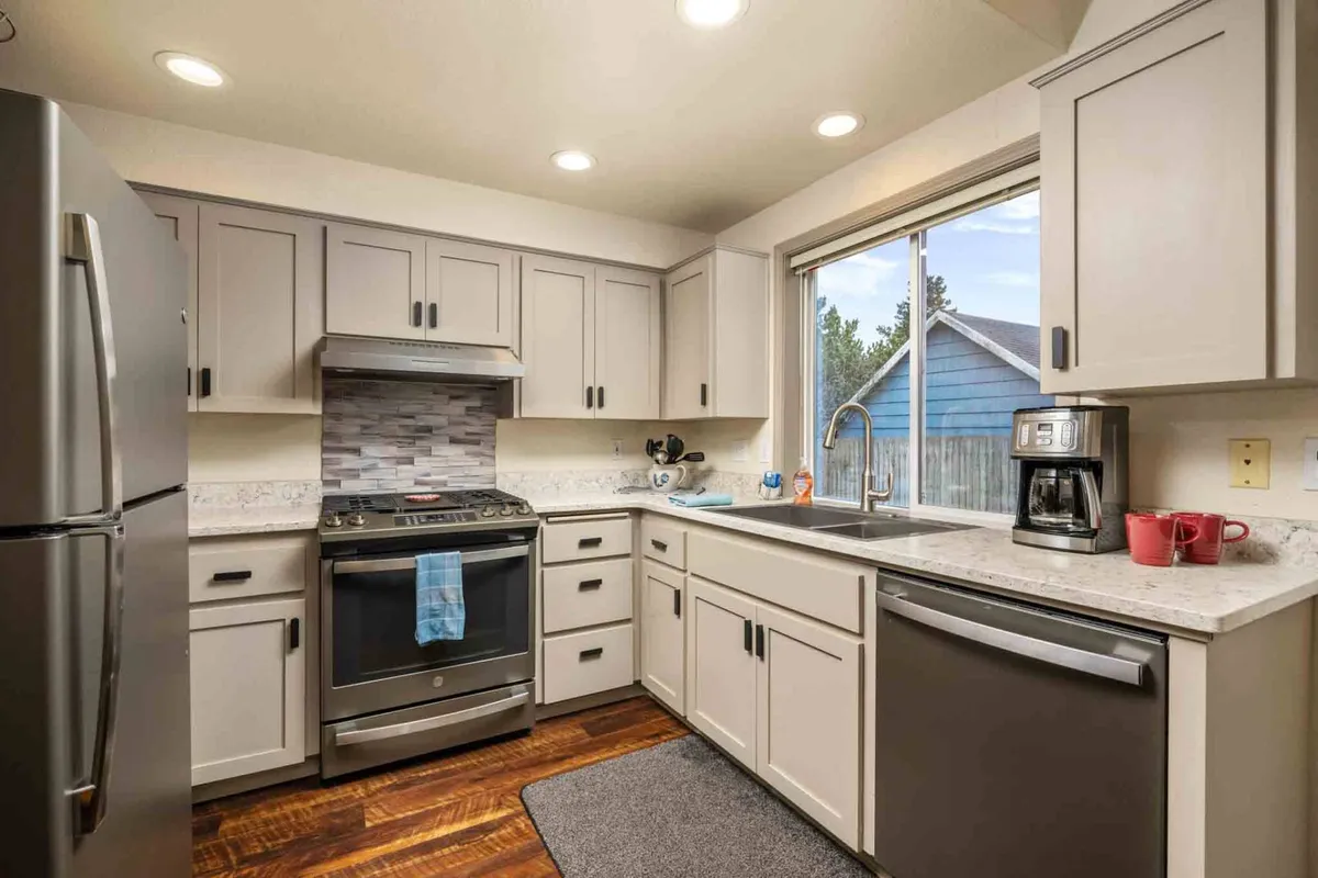 A bright, modern kitchen with stainless steel appliances, an inviting kitchen island, a window letting in ample natural light, and a coffee maker set on the counter. The space feels cozy and is clearly designed for both cooking and socializing over breakfast or coffee.