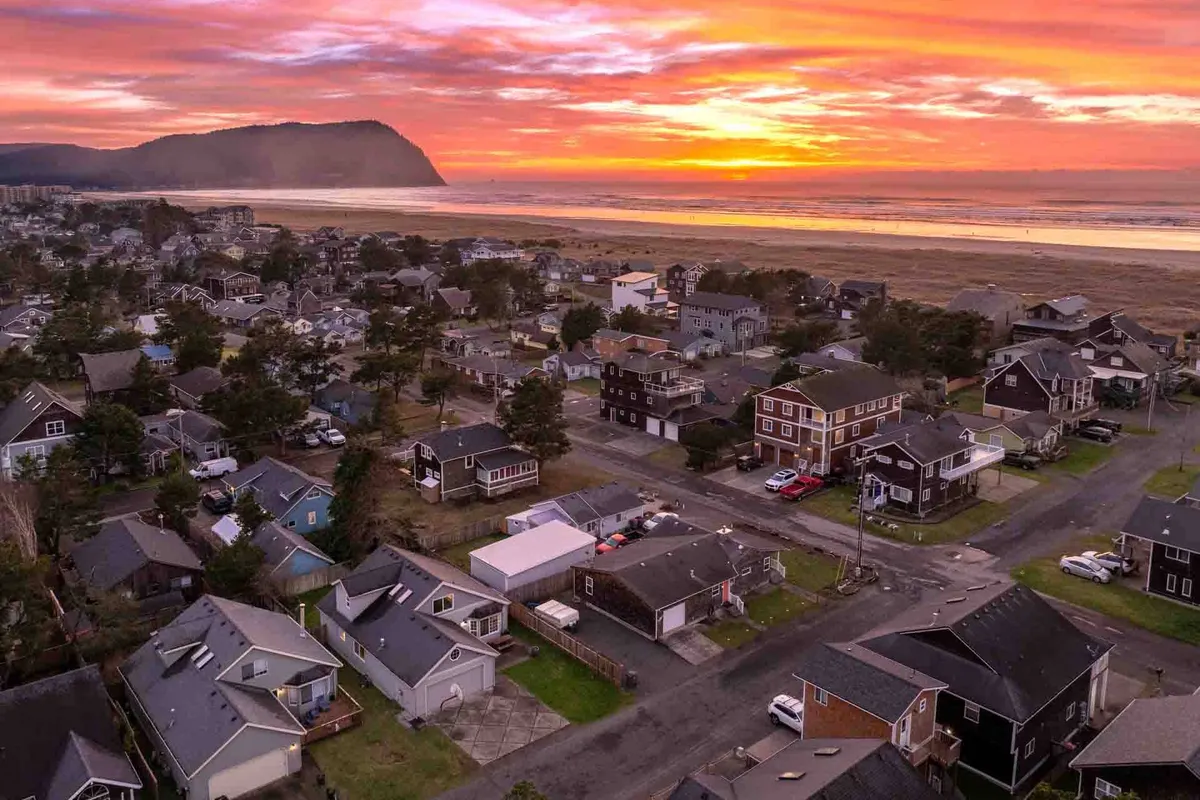 This inviting scene shows a serene beach at sunset, with the gentle waves lapping at the shore, homes nearby, and a majestic mountain in the distance. The ambiance is peaceful and perfect for family activities like beach walks, kite flying, or simply soaking in the view.