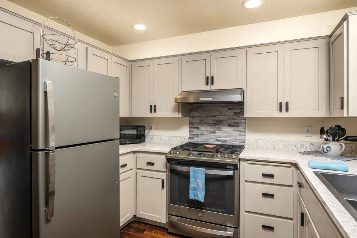 A welcoming kitchen scene featuring a stainless steel refrigerator, an oven with a stovetop, granite countertops, and sleek modern cabinetry. The layout signals practical efficiency and a space ready for meal prep or entertaining guests.