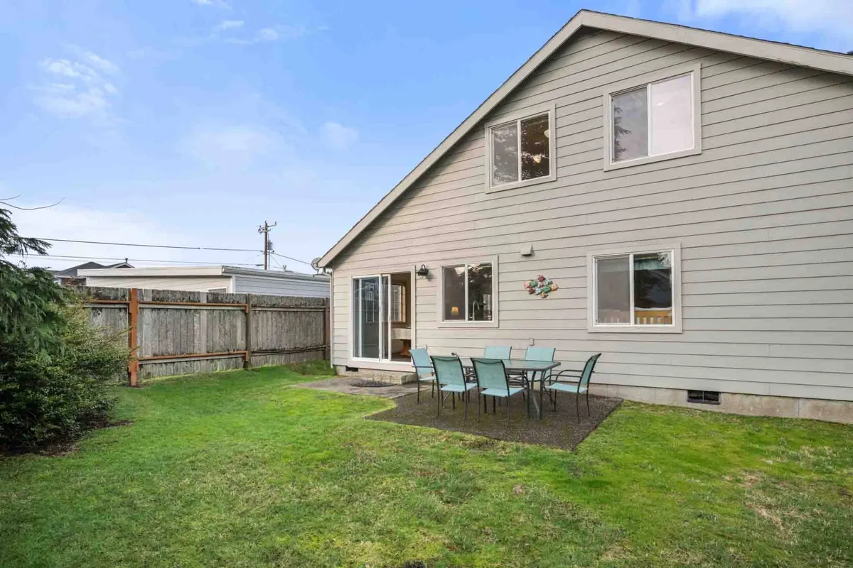 A lush, green lawn stretches out behind the home, anchored by a patio area featuring a table and chairs. The sliding glass door to the house suggests easy flow between indoors and outdoors, while the fenced yard provides a secure, private space for safe play. The setup is ideal for family meals, lively games, and outdoor relaxation.