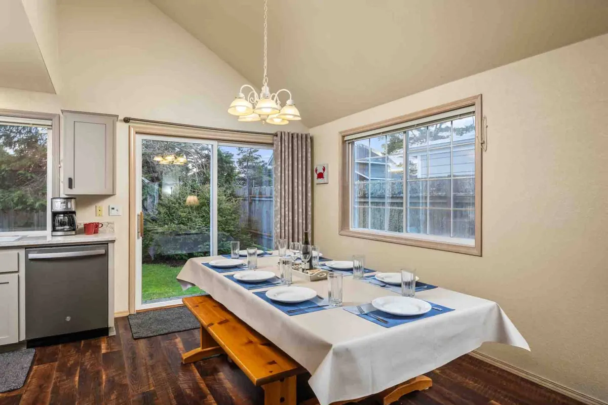 An inviting dining area with a table set for a meal, large windows offering views of the garden, and the kitchen visible in the background. The mood is homey and perfect for family meals or special occasions.