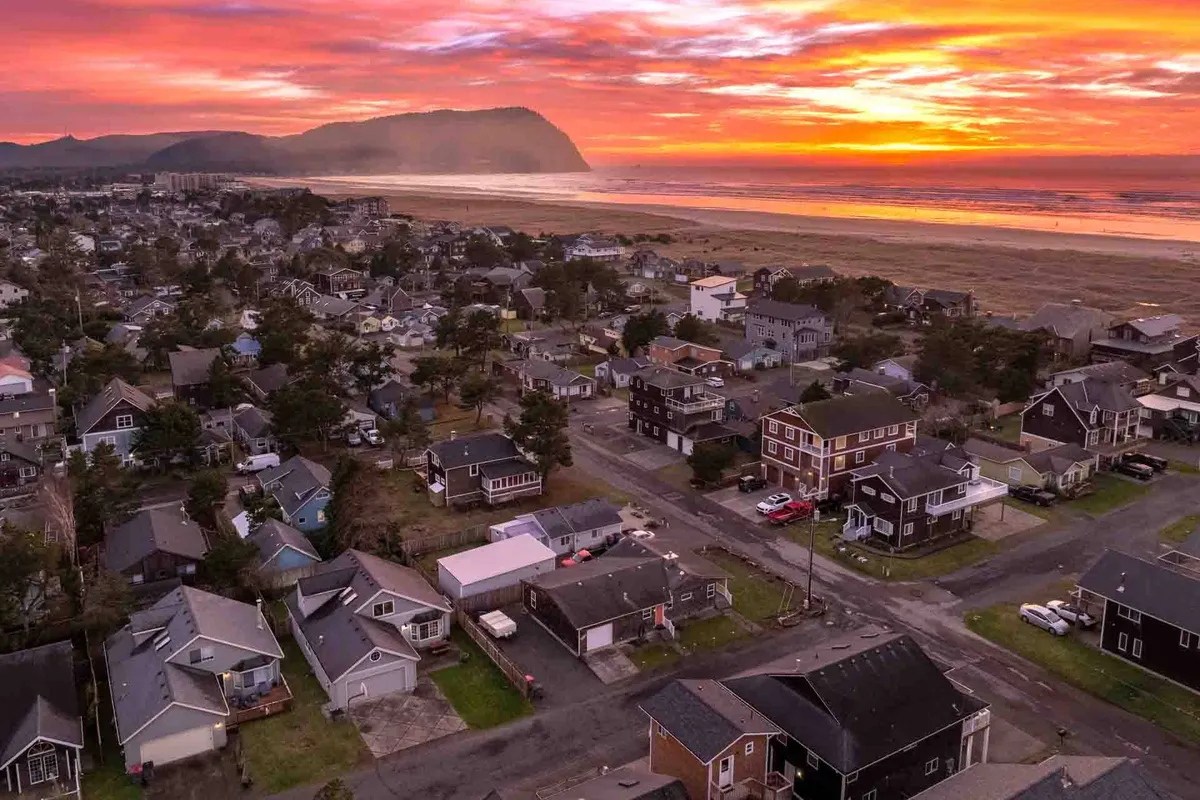 This wide-angle view showcases a peaceful coastal neighborhood as the sun sets, with pastel colors in the sky and houses nestled along the landscape—suggesting a welcoming community and tranquil place to return to after a day of adventure.