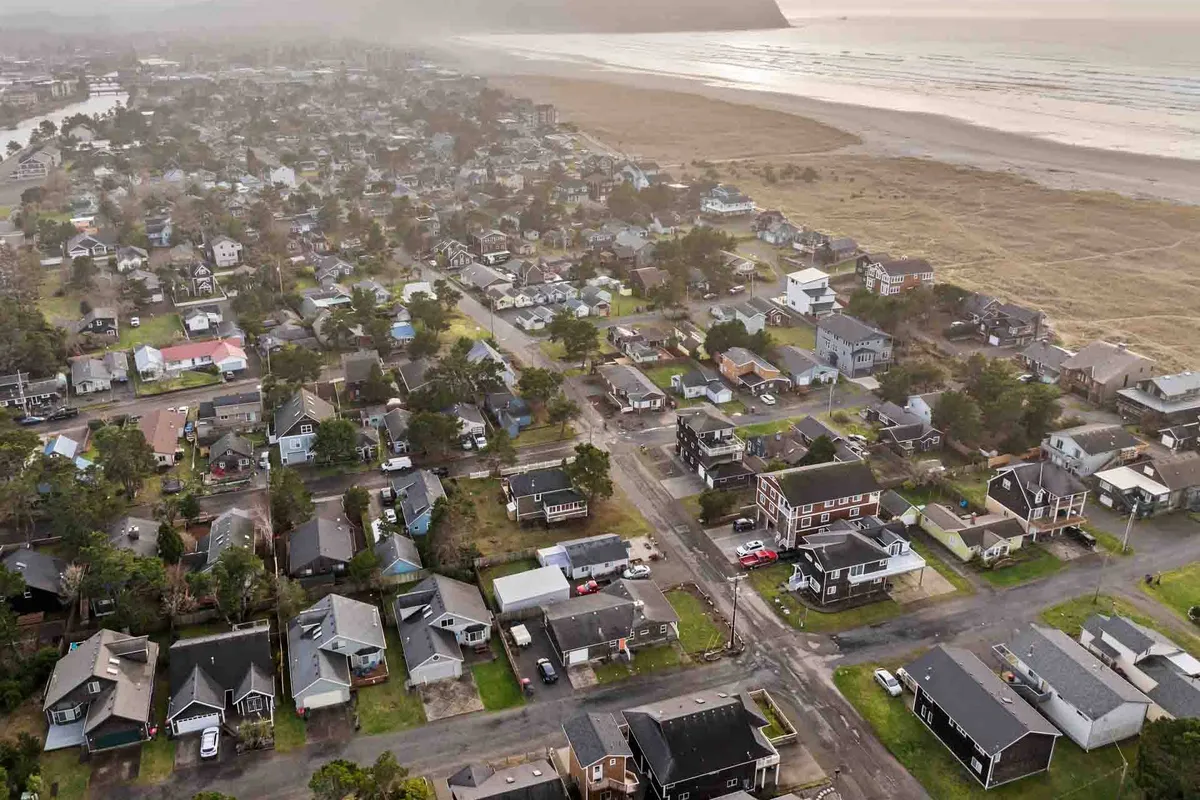 A peaceful residential neighborhood is shown adjacent to a broad, inviting beach and open fields. The setting sun casts a golden glow over both the homes and the nearby shoreline, highlighting how the community backs right up to the sand.