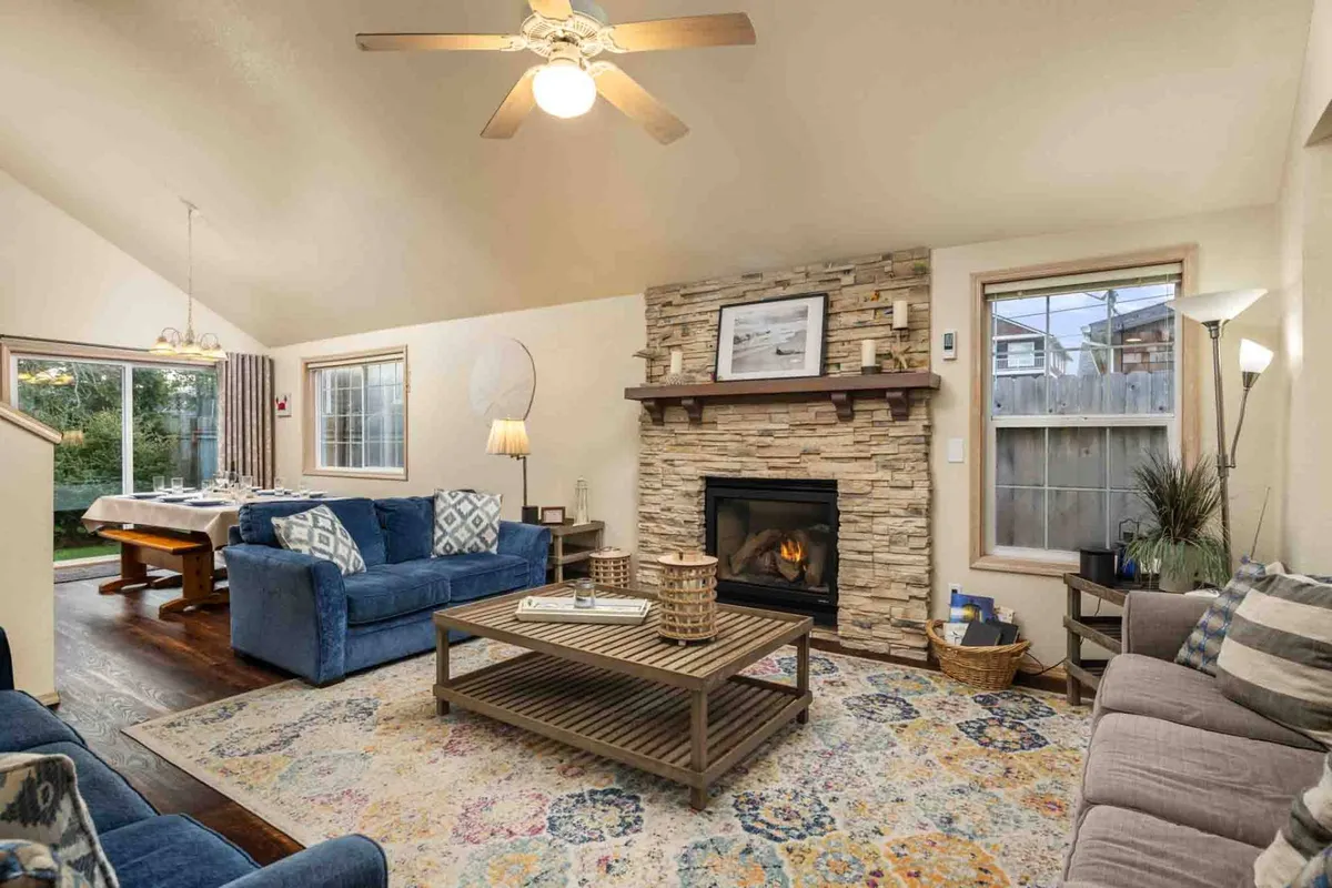 The image shows a warm and inviting living area featuring a glowing fireplace, a plush sofa, a stylish coffee table, and a bright dining space—perfect for gathering with family or friends. The ambience is cozy and welcoming, encouraging relaxation and socializing.